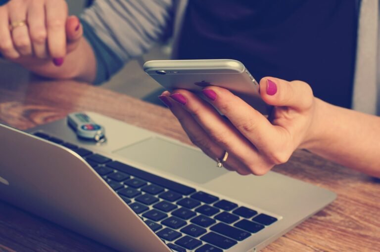 Person holding a smartphone while working on a laptop, representing website visibility and SEO troubleshooting